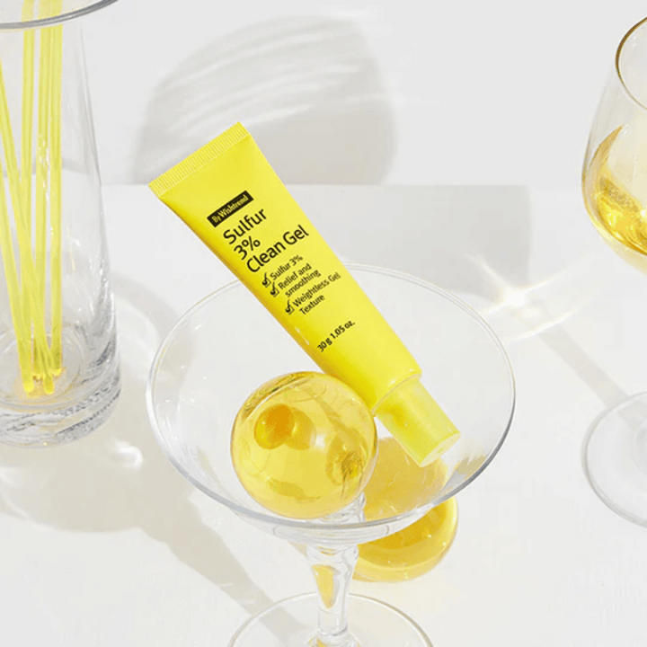 By Wishtrend Sulfur 3% Clean Gel v žltej tube umiestnený v koktailovom pohári so žltou sférou, obklopený elegantnými pohármi na bielom pozadí.