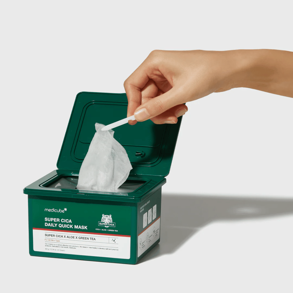 Zelená nádoba s otvoreným vekom ukazuje medicube Super Cica Daily Quick Mask. Ruka vyťahuje plachtovú masku s priloženou pinzetou. Produkt obsahuje Cica, aloe a zelený čaj, ideálny pre rýchlu hydratáciu a upokojujúci účinok.