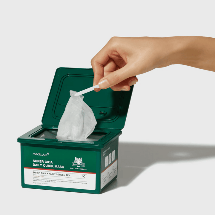 Zelená nádoba s otvoreným vekom ukazuje medicube Super Cica Daily Quick Mask. Ruka vyťahuje plachtovú masku s priloženou pinzetou. Produkt obsahuje Cica, aloe a zelený čaj, ideálny pre rýchlu hydratáciu a upokojujúci účinok.