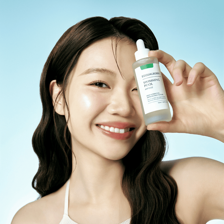 Usmievajúca sa žena drží Eqqualberry Swimming Pool Ampoule, produkt starostlivosti o pleť na intenzívnu hydratáciu, pred svetlomodrým pozadím.