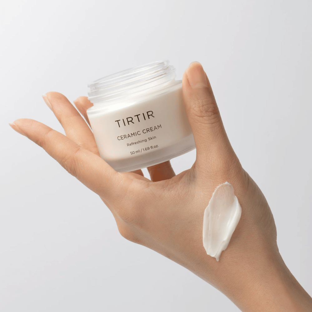 Ruka drží pohár s TIRTIR Ceramic Cream. Na chrbte ruky je nanesené množstvo krému. Krém sa zdá byť hustý a hydratačný. Balenie uvádza, že obsah je určený na "Refreshing Skin" a množstvo je 50 ml / 1.69 fl oz.