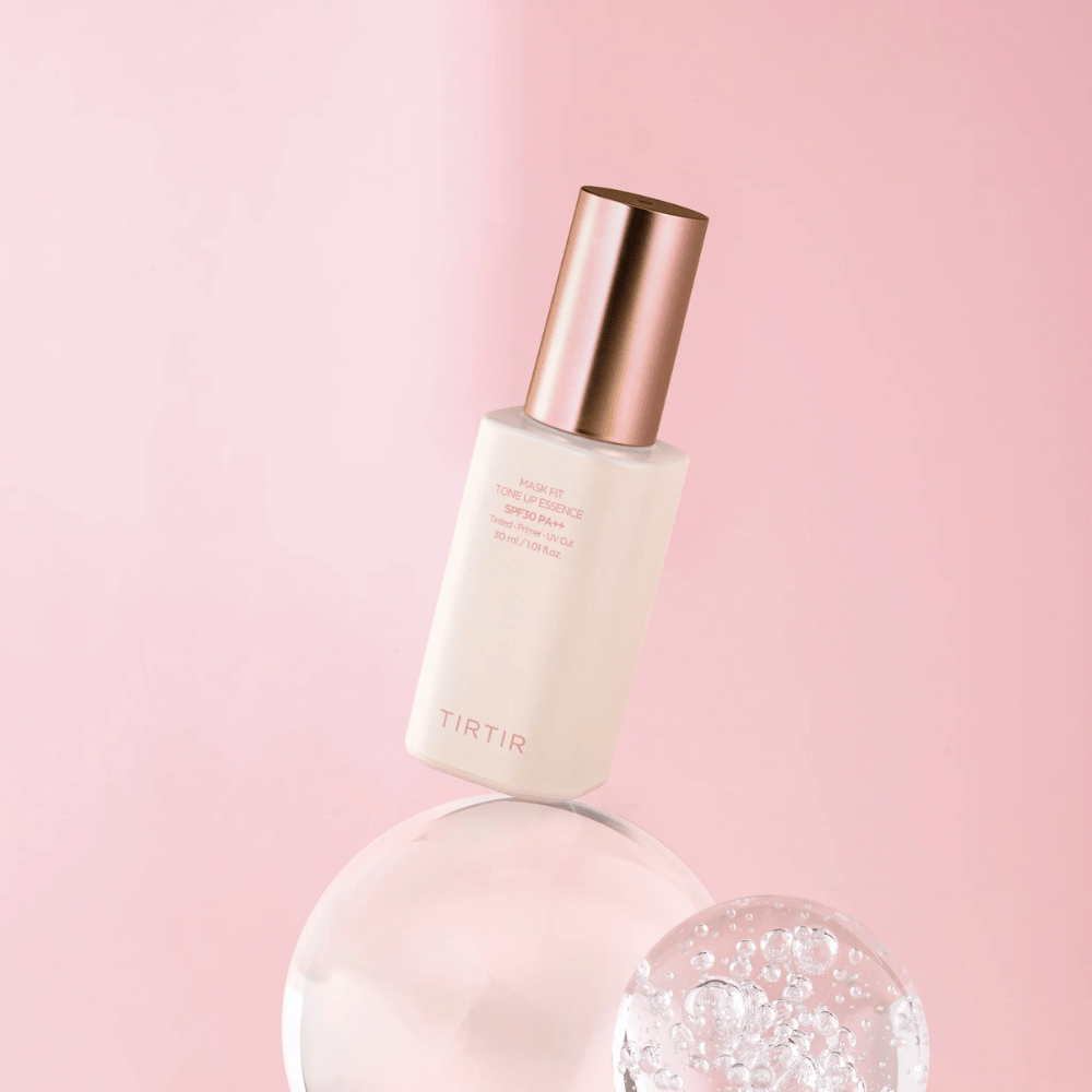 Obrázok ukazuje fľašu "TIRTIR MASK FIT TONE UP ESSENCE" s SPF30 PA++ na ružovom pozadí, čo vytvára pocit jemnosti a ženskosti.