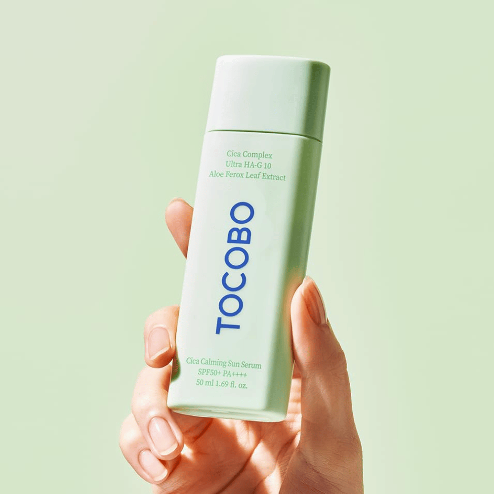 Ruka drží TOCOBO Cica Calming Sun Serum v mätovo zelenom balení s modrým textom na svetlozelenej pozadí.