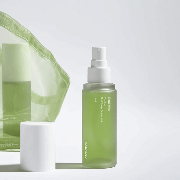 Fľaša s Celimax Noni Mist, zelená striekacia fľaša s bielym čerpadlom, stojí vedľa uzáveru. Produkt je zabalený v priehľadnom plastovom vrecku a je propagovaný ako Noni Energy Ampule Mist.