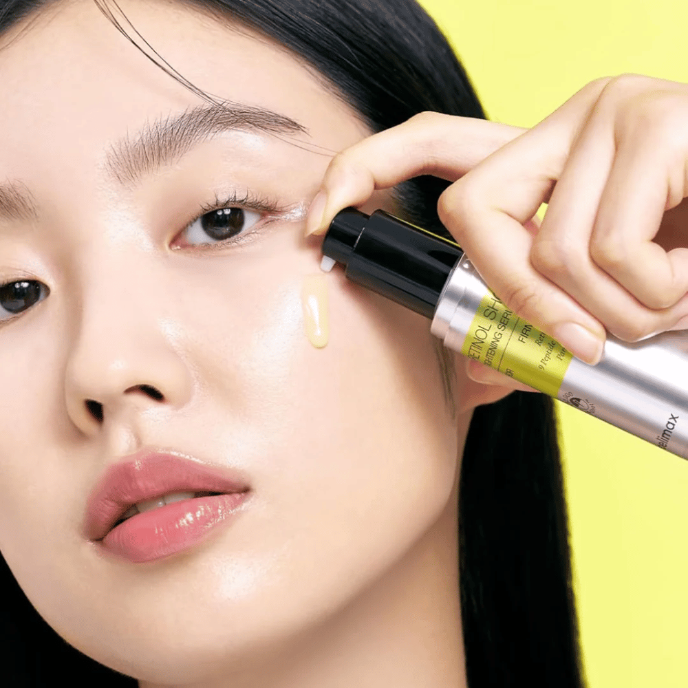 Modelka aplikuje The Vita-A Retinol Shot Tightening Serum od Tiam v blízkosti očného okolia, so zameraním na lesk pokožky a žltú konzistenciu séra.