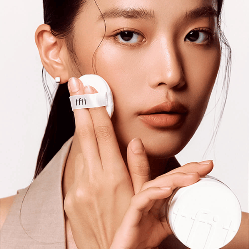 Žena aplikuje TFIT Translucent Set Finishing Powder #02 Skin Beige s púdrikom, drží bielu púderovú dózu s logom TFIT.