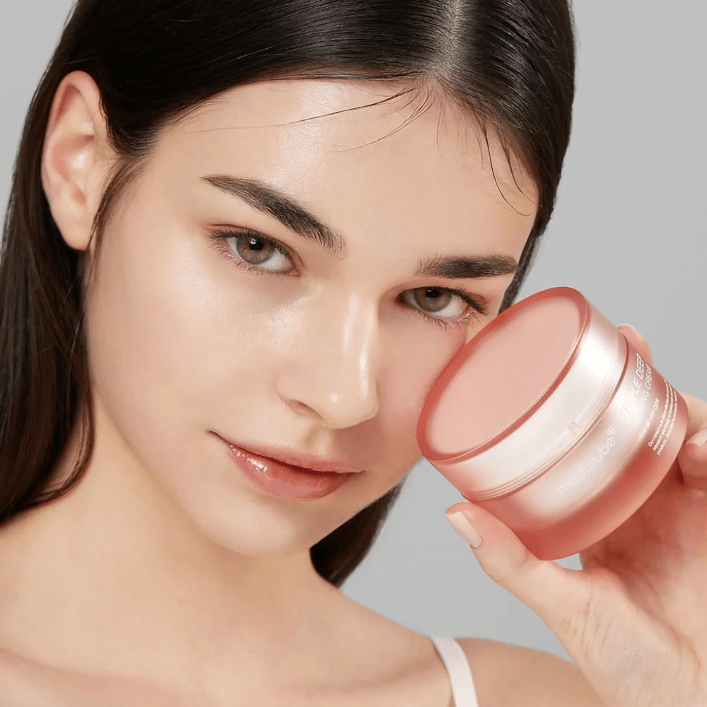 Obrázok zobrazuje ženu, ktorá drží nádobu s Triple Collagen Cream. Krém je navrhnutý na zlepšenie elasticity a hydratácie pokožky. Ženina pokožka vyzerá hladko a dobre udržiavaná.




