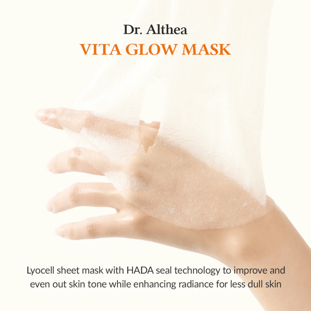 Ruka drží lyocellovú plátenú masku od Dr. Althea Vita Glow Mask. Maska zlepšuje žiarivosť a rovnomernosť pokožky s technológiou HADA Seal.