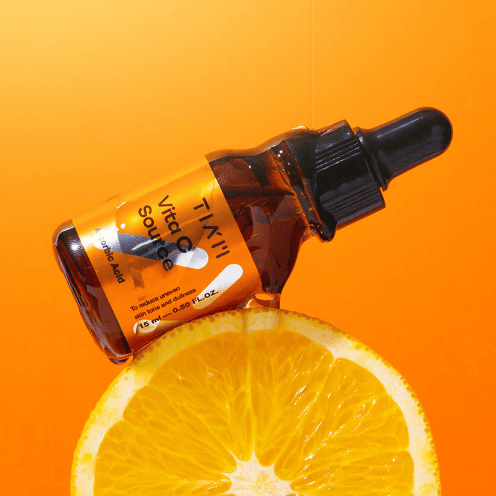 Fľaša TIA'M Vita C Source umiestnená proti pomaranču a oranžovému pozadiu, symbolizujúca sviežosť a antioxidačný účinok vitamínu C.