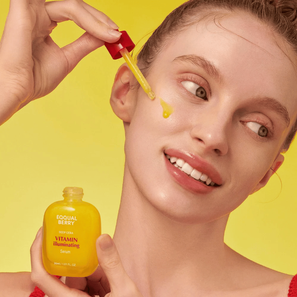 Usmievavá žena aplikuje Equal Berry Vitamin Illuminating Serum s pipetou. Svieža a žiarivá pleť na živom žltom pozadí, ktoré zodpovedá farbe séra.