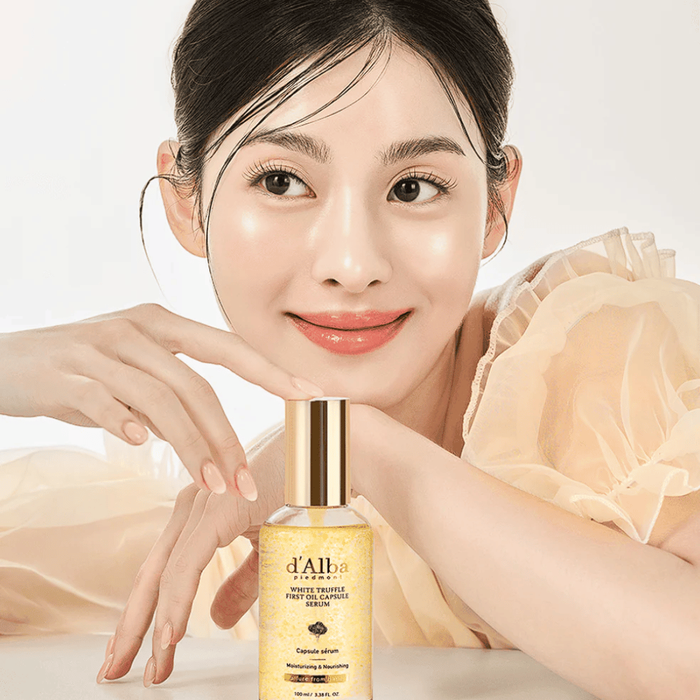 Modelka v svetlých šatách sa jemne usmieva vedľa d'Alba White Truffle First Oil Capsule Serum.