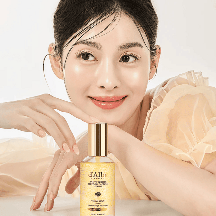 Modelka v svetlých šatách sa jemne usmieva vedľa d'Alba White Truffle First Oil Capsule Serum.