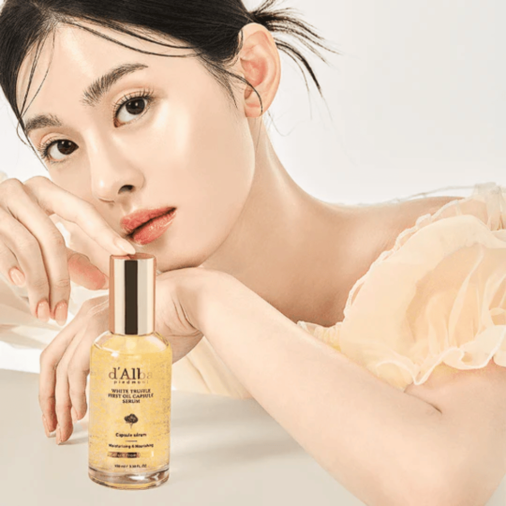 Modelka so žiarivou pokožkou pózuje vedľa d'Alba White Truffle First Oil Capsule Serum.