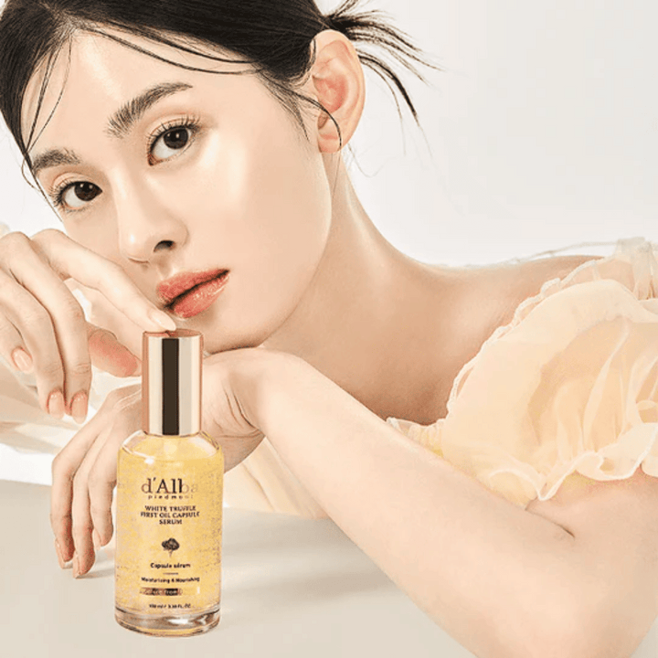 Modelka so žiarivou pokožkou pózuje vedľa d'Alba White Truffle First Oil Capsule Serum.