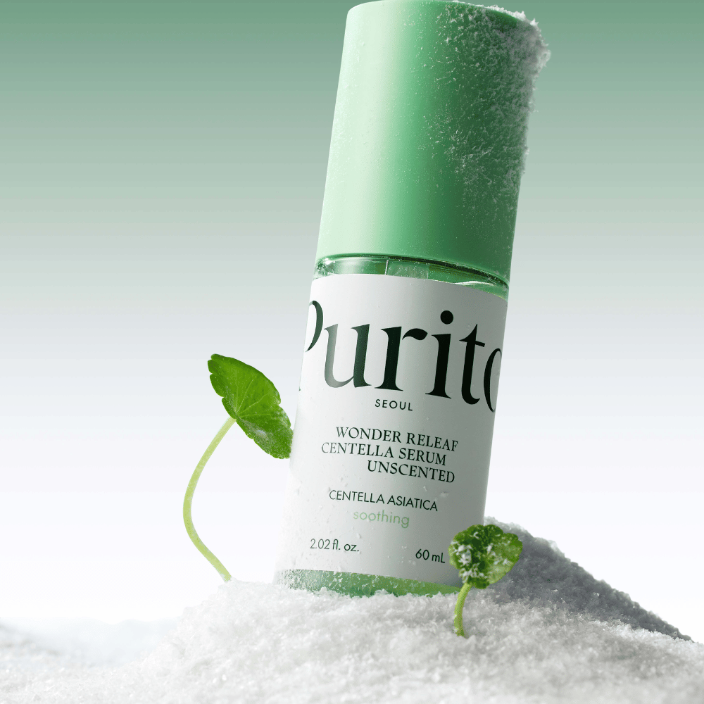 Fľaša s Purito Centella Serum leží v snehu, vidieť zelené listy, na jemnom zelenom pozadí.
