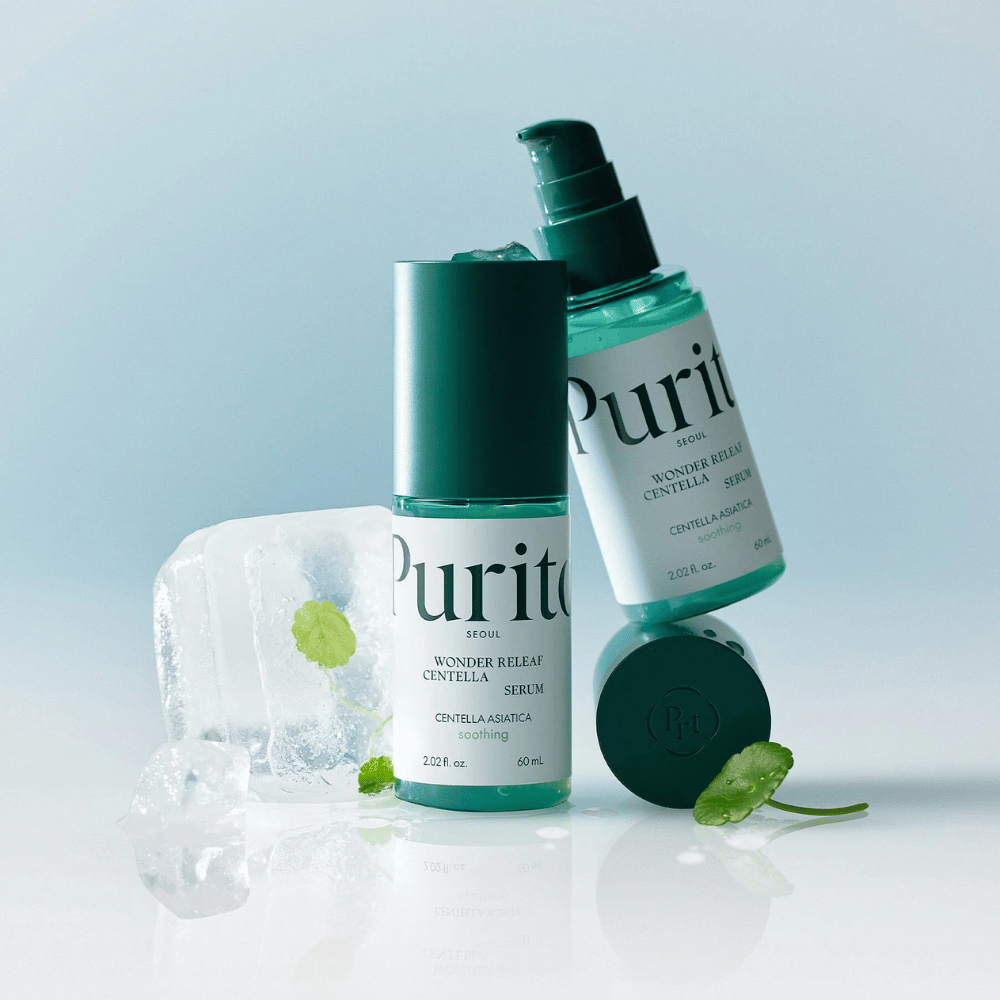Dve fľaše Purito Wonder Releaf Centella Serum, jedna stojaca a jedna ležiaca, obklopené kúskami ľadu s listami centelly a voľným listom na svetlomodrom povrchu.