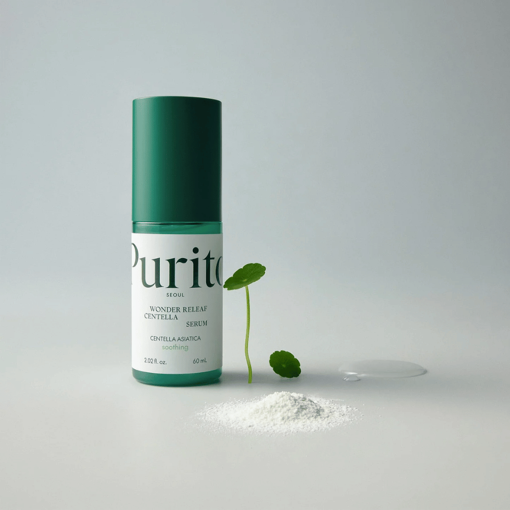 Zelená fľaša Purito Wonder Releaf Centella Serum 60 ml stojí na bielom podklade, obklopená listami centelly, priehľadnou kvapkou séra a malým bielym práškom.