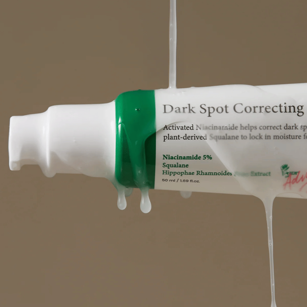 Detailný záber na pumpovaciu fľašku Axis-Y Dark Spot Correcting Glow Serum s bielym obalom a zeleným uzáverom, pokrytú tečúcou priehľadnou tekutinou.