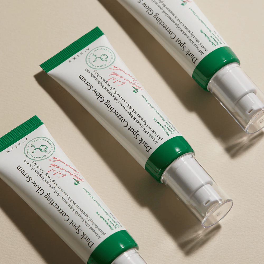 Tri tuby Axis-Y Dark Spot Correcting Glow Serum so zeleným uzáverom a bielym obalom ležia na svetlom podklade.