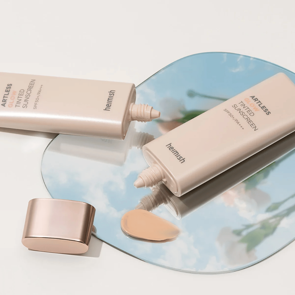 Fľaša heimish Artless Glow Tinted Sunscreen SPF50+ PA+++ 40ml a fľaša korektora na zrkadle, ktoré ukazujú rôzne odtiene pokožky.