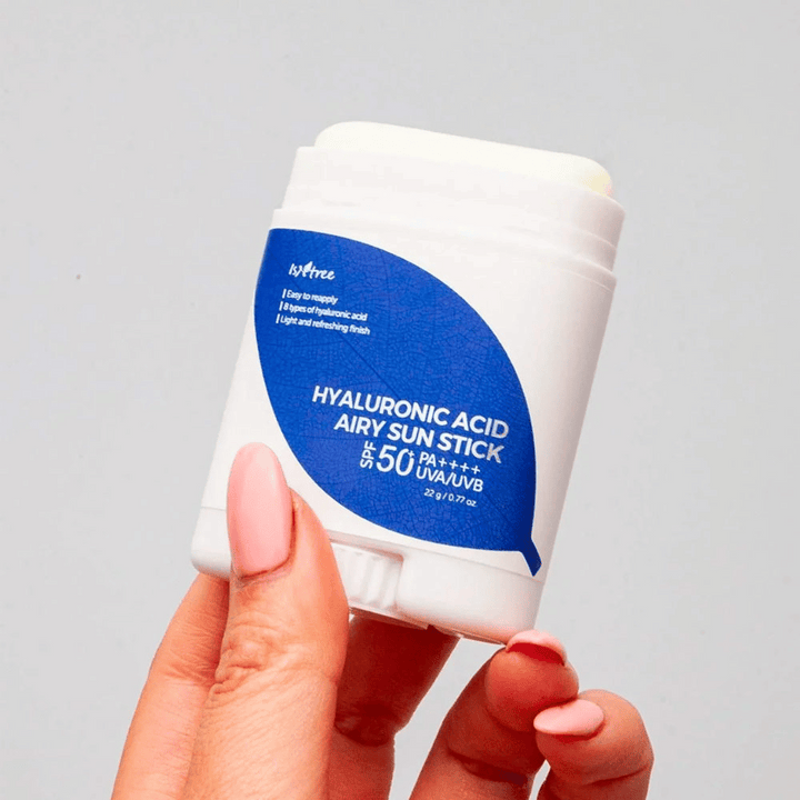 Ruka drží bielu slnečnú tyčinku s modrou etiketou od značky Isntree. Produkt sa volá "Hyaluronic Acid Airy Sun Stick" a má ochranný faktor SPF 50+ PA++++.