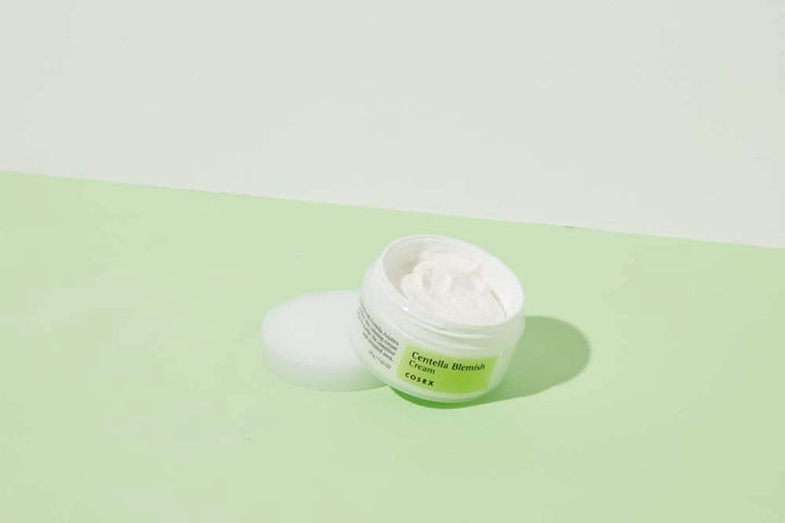 Nádoba COSRX Centella Blemish Cream 30ml, ktorá je umiestnená na zelenej ploche.