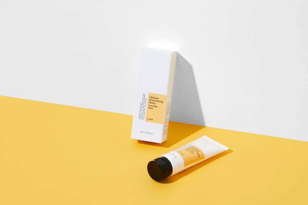 Tuba COSRX Ultimate Moisturizing Honey Overnight Mask 60ml pre podráždenú pokožku na žltom pozadí.