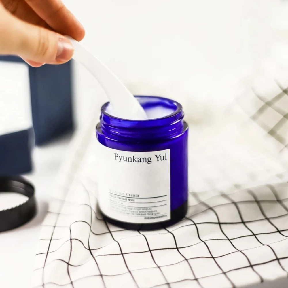 Osoba používa pohár Pyunkang Yul Nutrition Cream 100ml na stole.