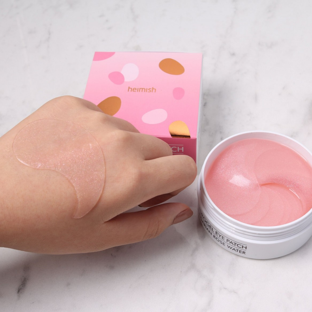 Ruka, ktorá drží ružový Bulgarian Rose Hydrogel Eye Patch 60ks od heimish a aplikuje očnú masku.