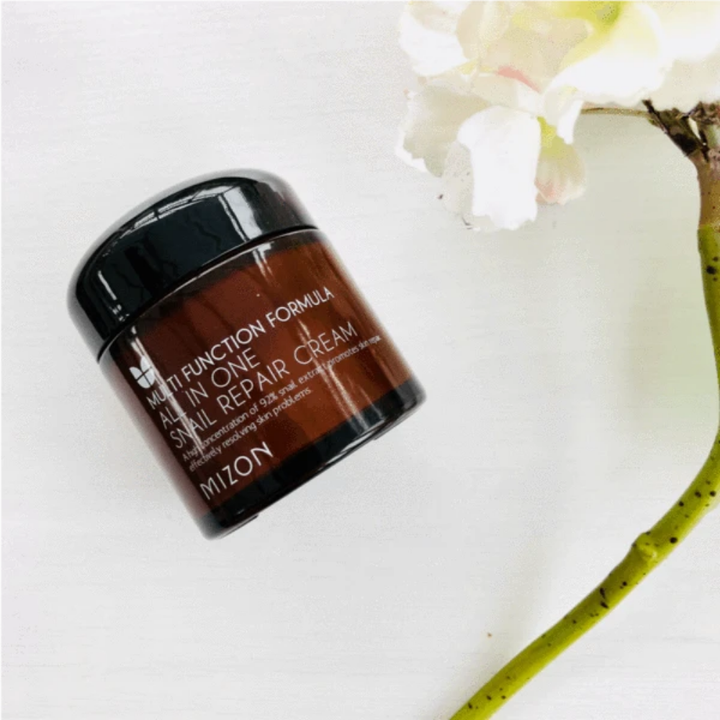 Nádoba MIZON All In One Snail Repair Cream 75ml vedľa kvetu.
