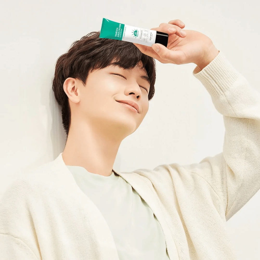 Mladý muž chráni svoju citlivú pleť pred UV žiarením tým, že drží tubu SOME BY MI Truecica Aqua Calming Sun Cream 50ml na hlave.