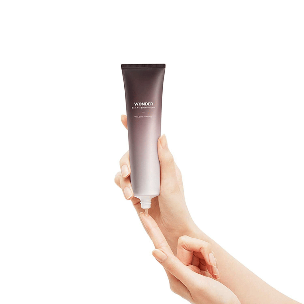 Ruka ženy, ktorá drží tubu Haruhuru Wonders Black Rice Soft Peeling Gel 100 ml na bielom pozadí.