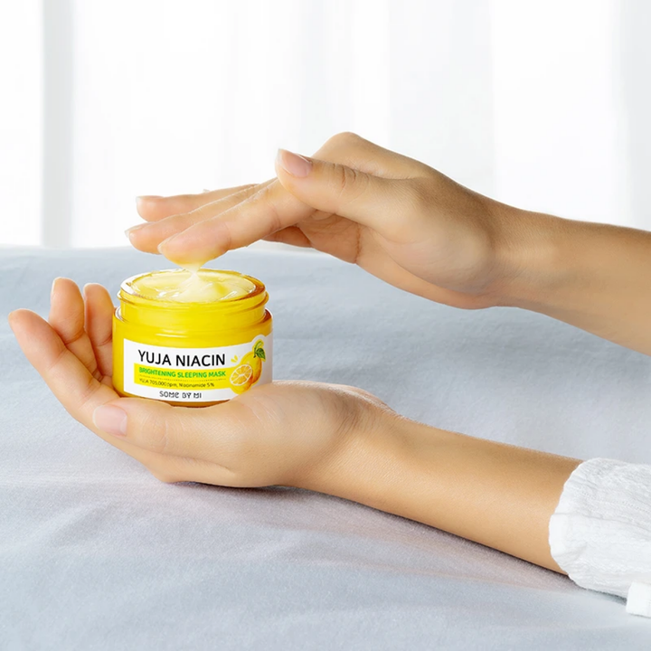 Ruka ženy držiaca nádobu s SOME BY MI Yuja Niacin Brightening Sleeping Mask 60g pre nerovnomerný tón pleti.