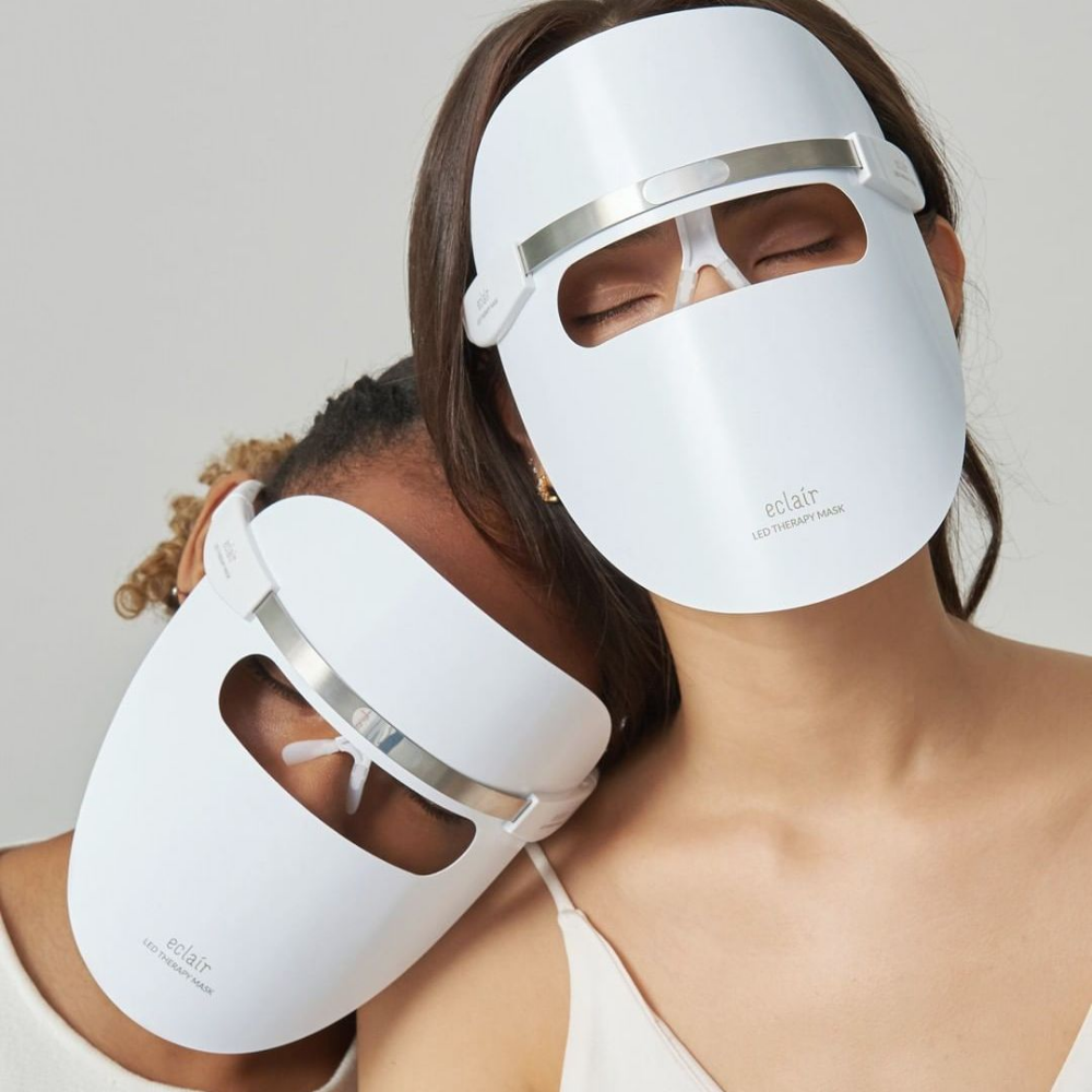 Dve ženy nosiace biele masky demonštrujú ECLAIR LED Therapy Mask na zlepšenie tónu pleti.