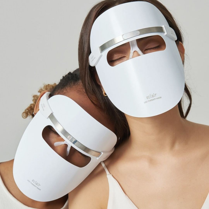Dve ženy nosiace biele masky demonštrujú ECLAIR LED Therapy Mask na zlepšenie tónu pleti.