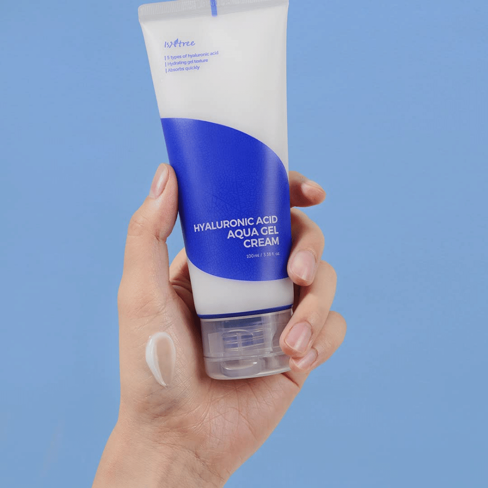 Ruka, ktorá drží tubu Isntree Hyaluronic Acid Aqua Gel Cream 100ml na modrom pozadí.